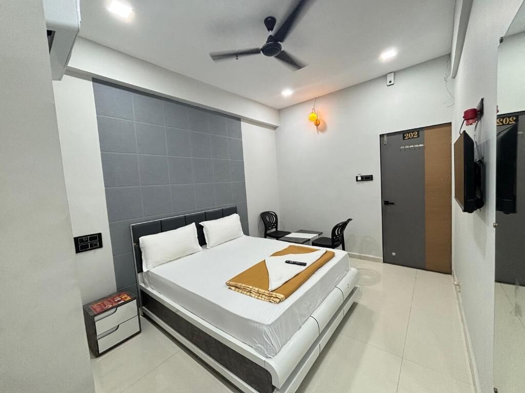 A modern hotel room with a bed, a desk, a chair, a ceiling fan, and a door.
