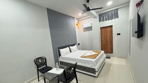 A bedroom with a bed, a desk, two chairs, a ceiling fan, and a TV mounted on the wall. - Hotel Mojito (Vyara)