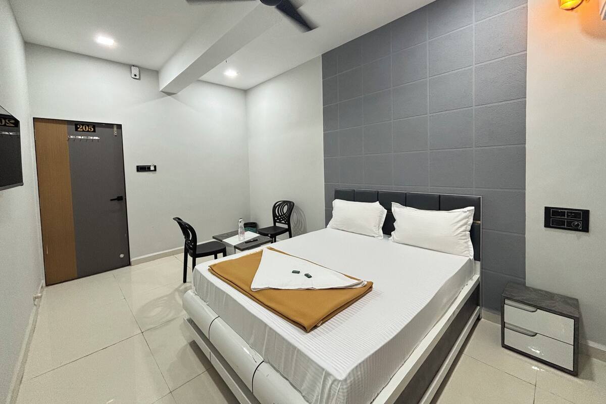 A hotel room with a bed, a desk, a chair, a ceiling fan, and a wall-mounted light.