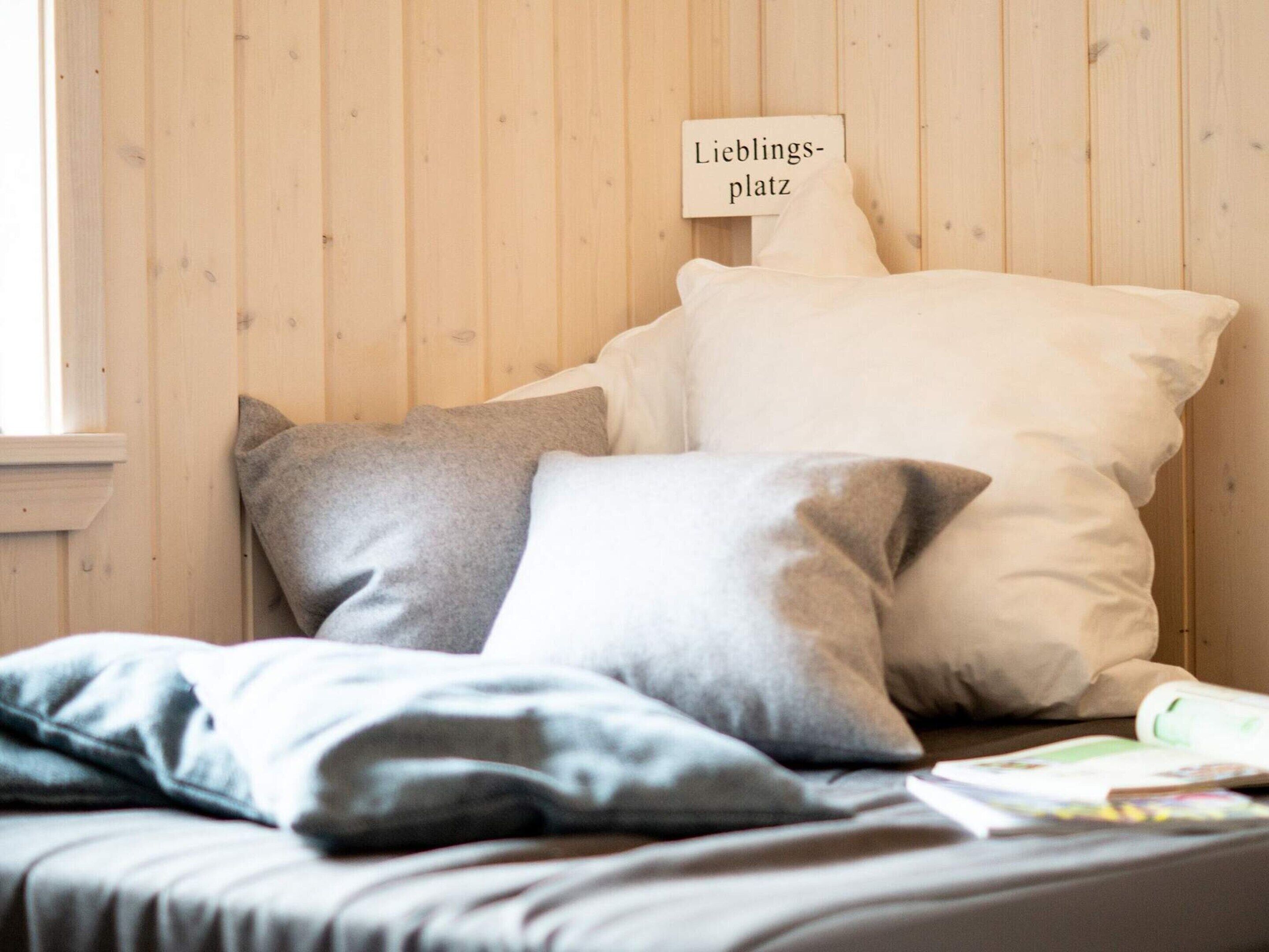 Un lit avec des oreillers et une pancarte sur laquelle on peut lire « Lieblings-platz », le tout adossé à un mur en bois.