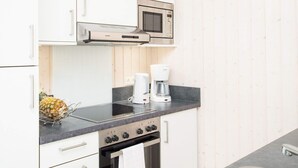 A kitchen with white cabinets, a stainless steel microwave, a Bosch coffee maker, and a stove. - 4 Star Holiday Home in Grossenbrode (Grossenbrode)