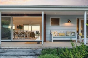 Ein modernes Haus mit einer überdachten Veranda, einem Essbereich mit Tisch und Stühlen sowie einem hellblauen Sofa mit Kissen.