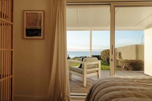 Ein Schlafzimmer mit einem Bett, einer Glasschiebetür, die zu einem Balkon mit einem Stuhl und Meerblick führt.