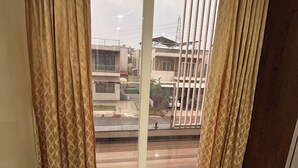 A room with a large window, a bed, and a view of buildings outside. - Luxury 4BHK Villa Near Airport, Hyderabad Family + Work Friendly (Hyderabad)