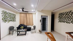 A living room with a sofa, two chairs, a coffee table, a decorative wall, a ceiling fan, and a door. - Luxury 4BHK Villa Near Airport, Hyderabad Family + Work Friendly (Hyderabad)