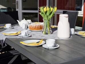 A table set for breakfast with a vase of yellow flowers, a teapot, a pitcher, and plates with utensils. - 4 Star Holiday Home in Grossenbrode (Grossenbrode)