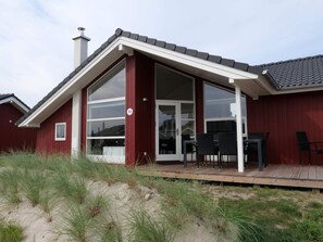 A red building with a large glass door and windows, a deck with chairs, and a number 72 sign. - 4 Star Holiday Home in Grossenbrode (Grossenbrode)
