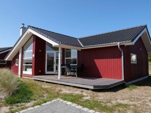 A red building with a covered patio, a glass door entrance, and a small table and chairs outside. - 4 Star Holiday Home in Grossenbrode (Grossenbrode)