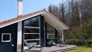 A modern house with a large deck, a chimney, and a glass door leading to a patio area. - 4 Star Holiday Home in Grossenbrode (Grossenbrode)