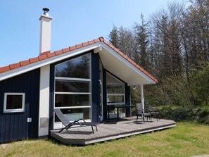 A modern house with a large deck, a chimney, and a glass door leading to a patio area. - 4 Star Holiday Home in Grossenbrode (Grossenbrode)