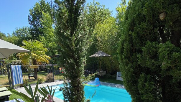 Une piscine entourée d’une végétation luxuriante, sous un ciel bleu et dégagé.