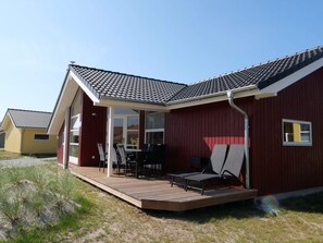 A single-story building with a covered patio, a dining area with chairs and a table, and a red exterior. - 4 Star Holiday Home in Grossenbrode (Grossenbrode)