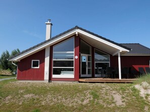 A red building with a large glass door, a chimney, and a deck with chairs. - 4 Star Holiday Home in Grossenbrode (Grossenbrode)