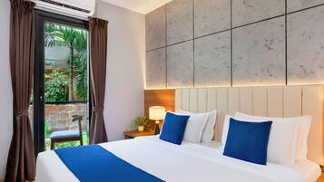 A hotel room with a bed, a nightstand, a lamp, and a view of greenery outside.