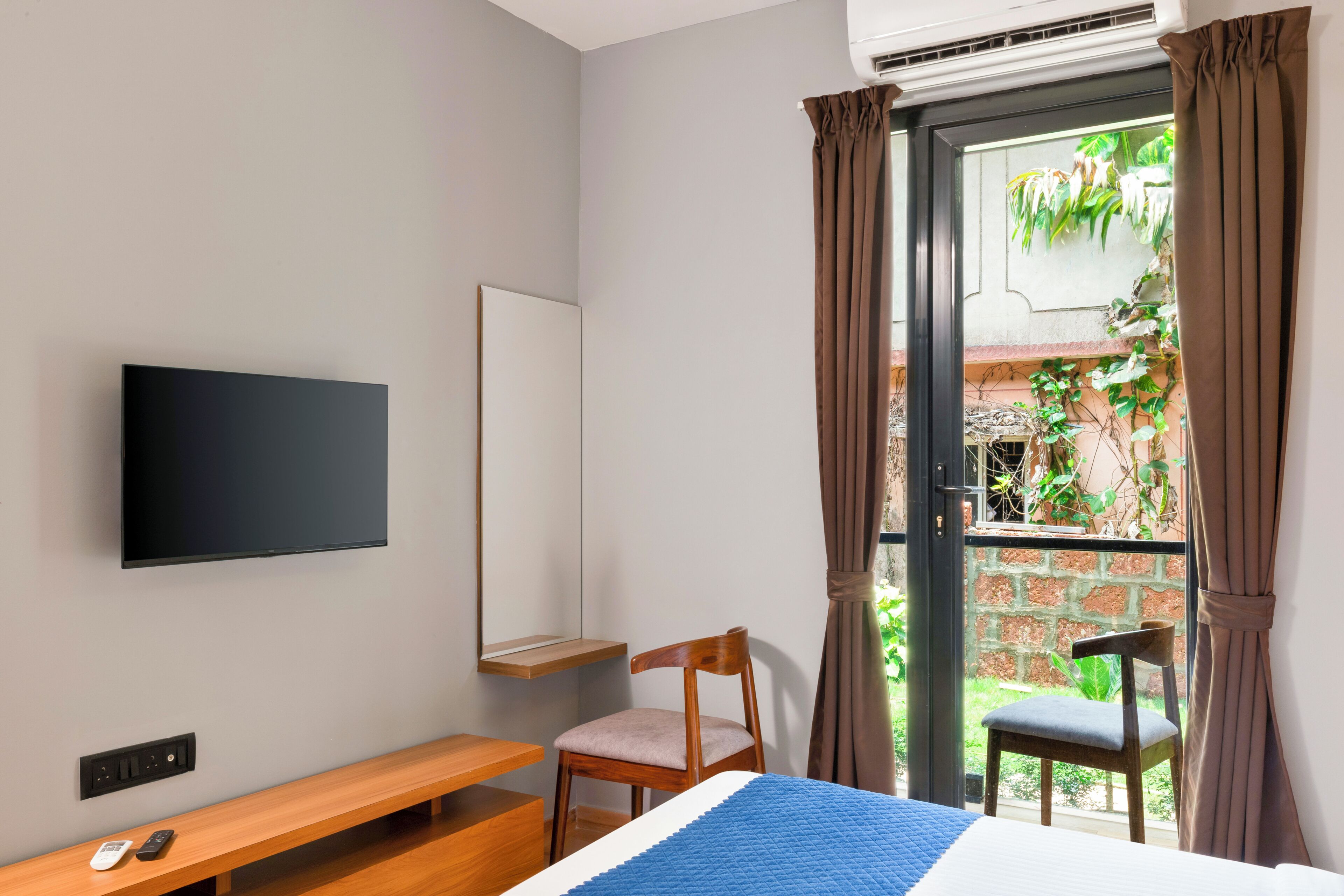 Un dormitorio con cama, televisor montado en la pared, un banco y una silla.