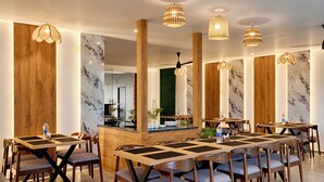 A modern dining area with wooden tables, cushioned chairs, and pendant lighting.