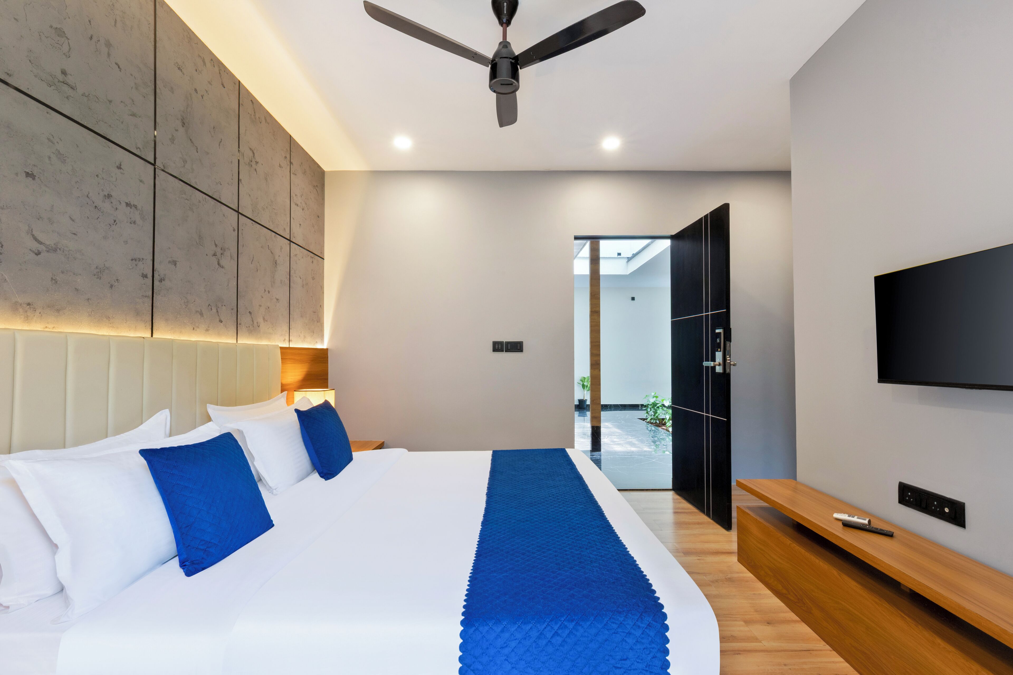 Una habitación de hotel moderna con una cama grande, un ventilador de techo, un televisor y un banco de madera.