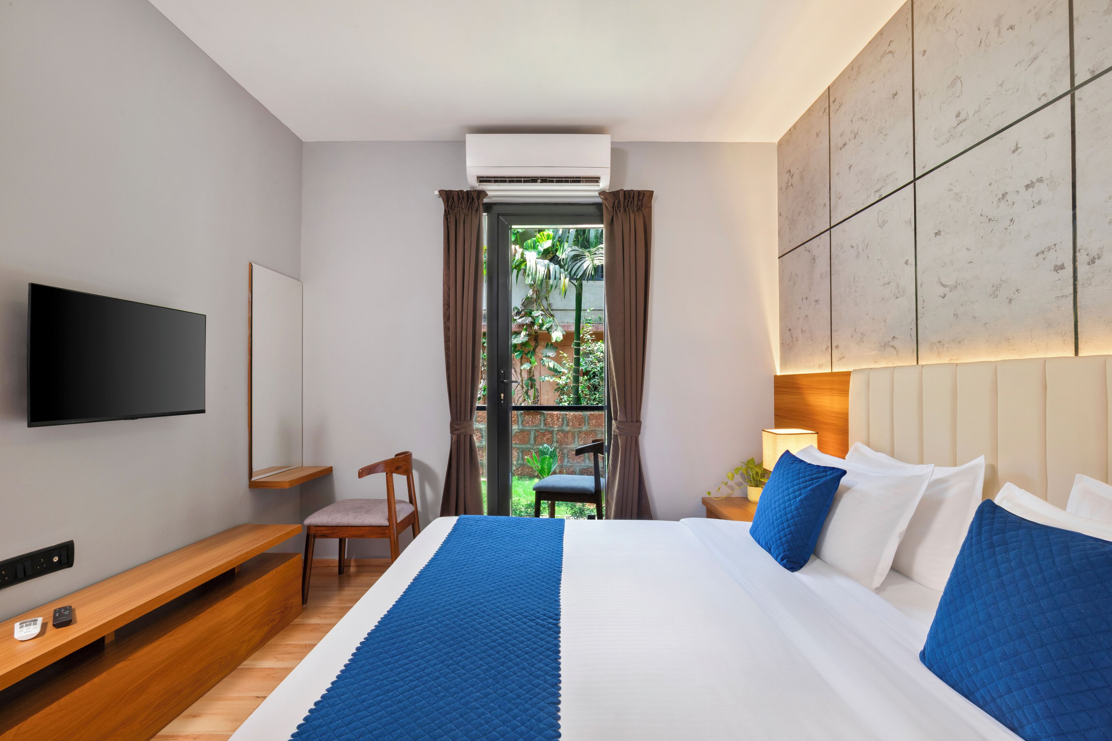 Habitación de hotel moderna con cama, televisor, zona de estar y vistas a zonas verdes.