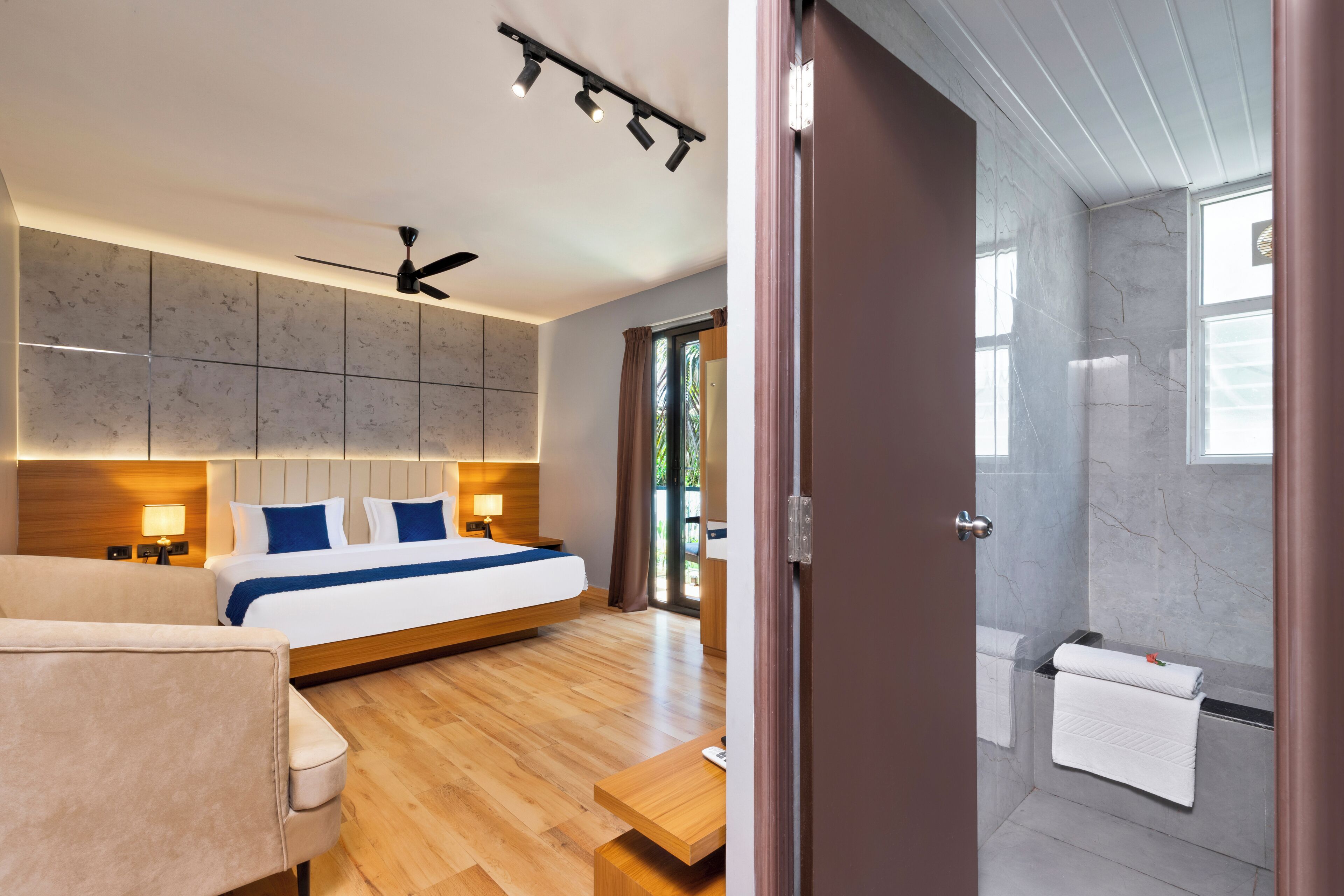 Une chambre d’hôtel moderne avec un grand lit, des lampes de chevet, un ventilateur de plafond et un plancher en bois.