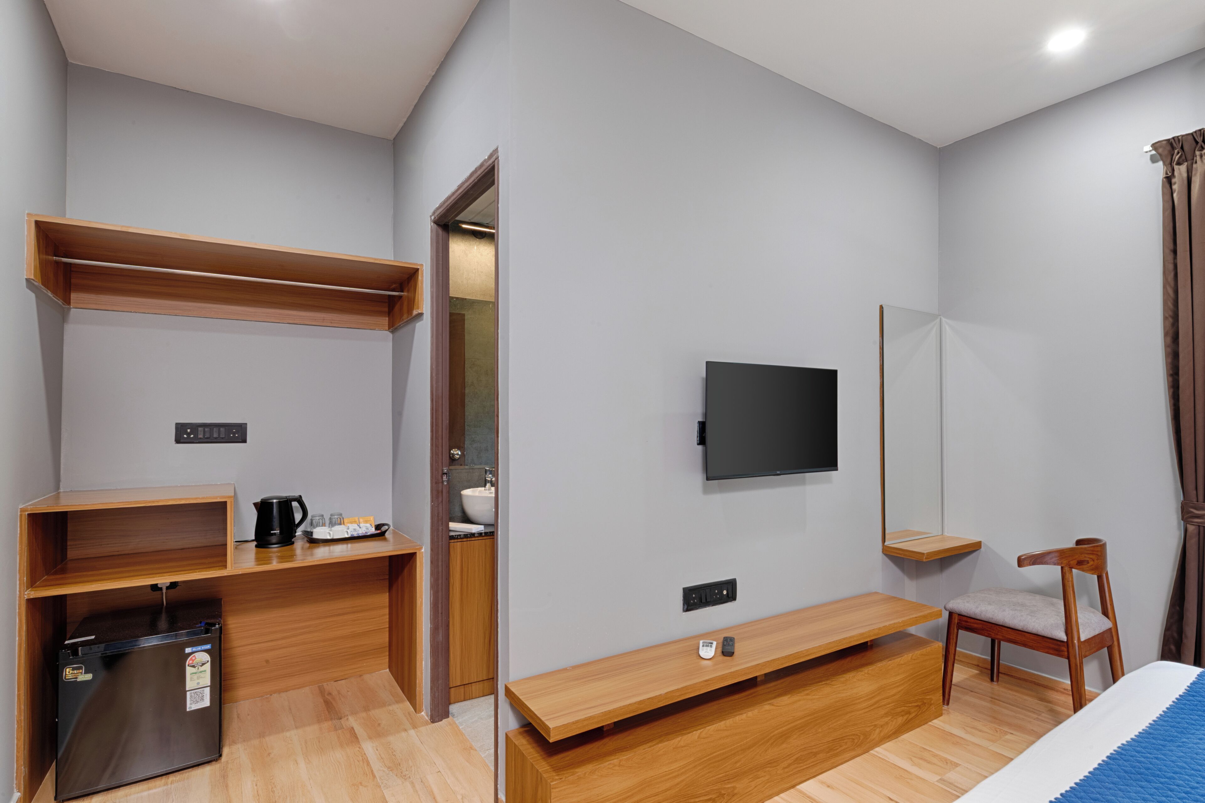 Een kleine hotelkamer met een bed, een televisie, een houten bureau, een stoel en een kleine koelkast.