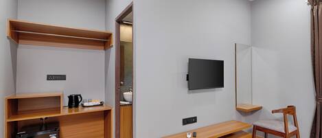 A compact hotel room with a bed, a TV, a wooden desk, a chair, and a small refrigerator.