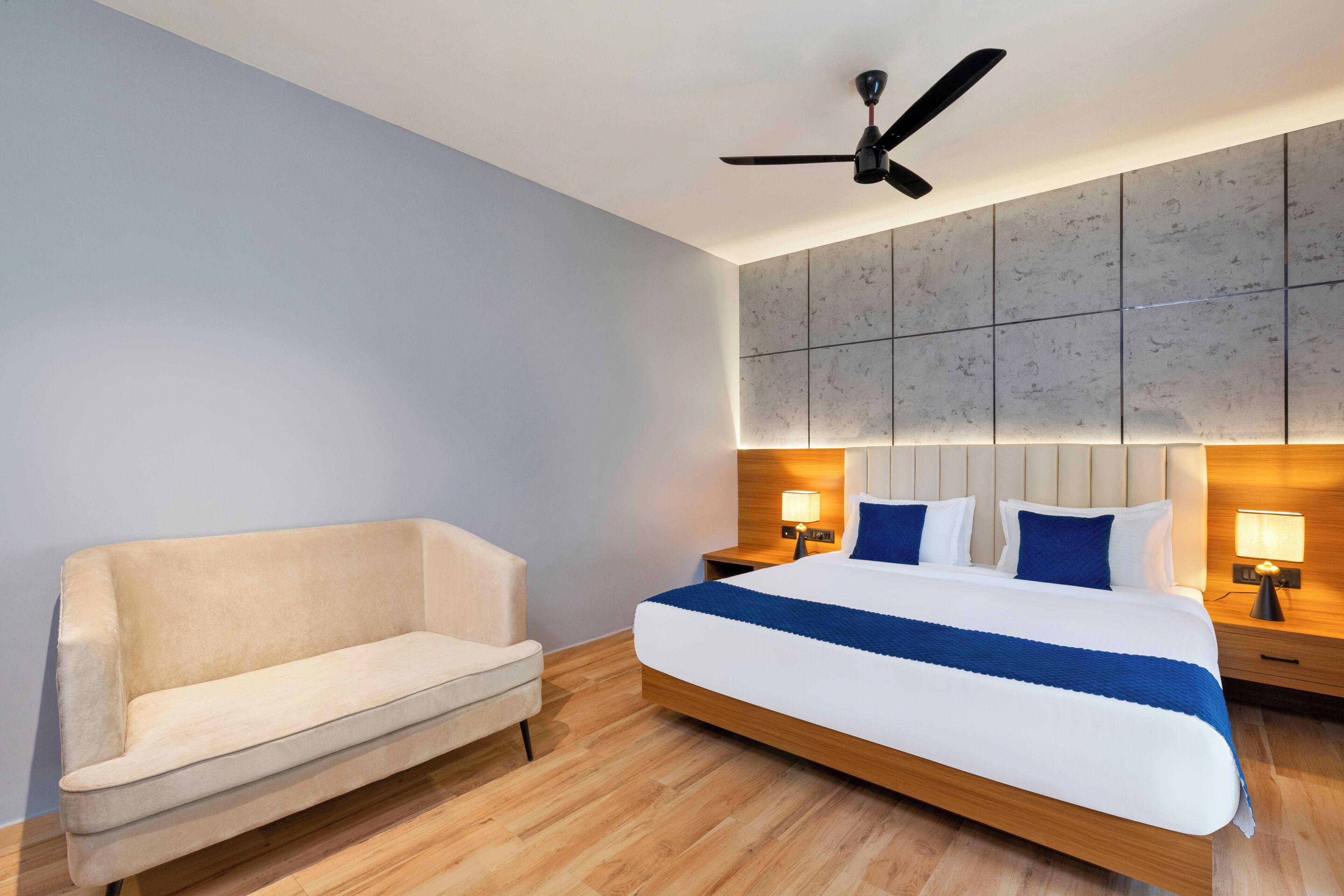 Ein Hotelzimmer mit Bett, Sofa, Deckenventilator und Wandleuchte.