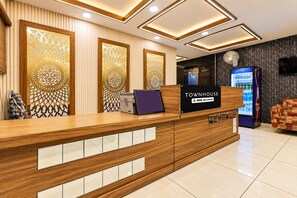A hotel reception desk with a wooden finish, a digital screen, and a sign indicating it is serviced by YOYO. - Deluxesaanvi Paradise (Bhopal)