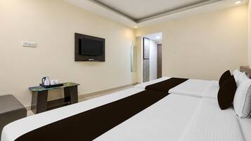 Une chambre d’hôtel avec un lit, un téléviseur fixé au mur, une petite table avec une machine à café et une porte donnant sur une autre pièce.