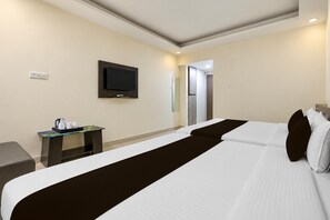 Habitación de hotel con cama, televisor montado en la pared, una mesita con cafetera y una puerta que conduce a otra habitación.