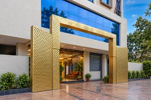 A modern building with a glass facade, a geometric entrance design, and a paved outdoor area with potted plants. - Deluxesaanvi Paradise (Bhopal)