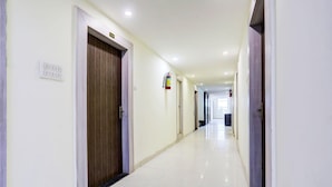 A long, well-lit hallway with doors on both sides, a fire extinguisher on the wall, and a light switch on the left.