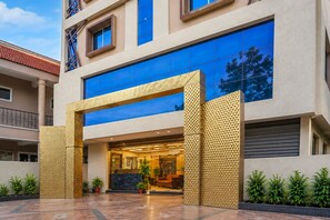 A modern building with a large glass entrance and a geometric golden structure in front. - Deluxesaanvi Paradise (Bhopal)