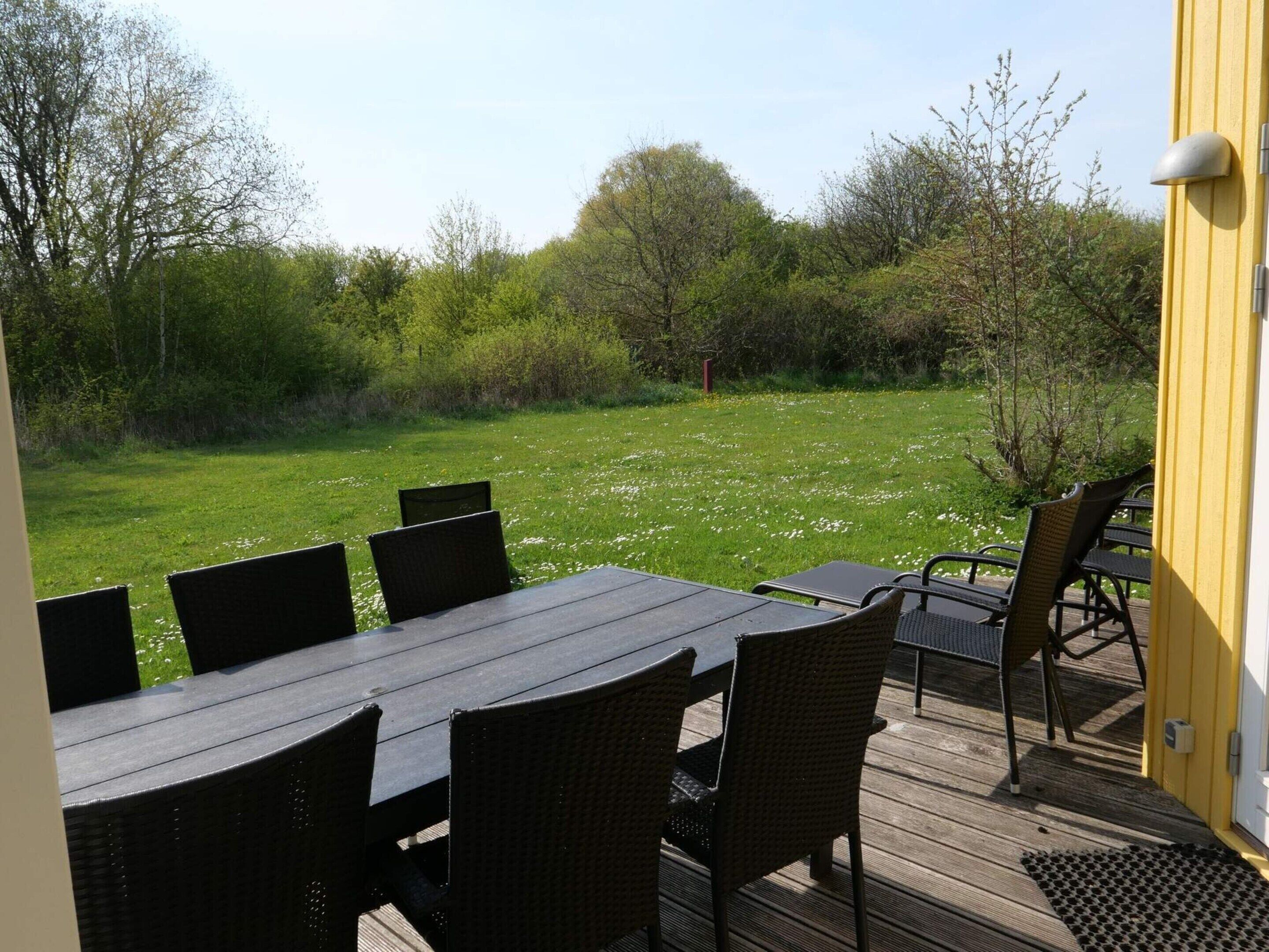 An outdoor dining area with a wooden deck, wicker chairs, and a table.