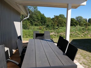 An outdoor patio with a wooden table and black chairs, surrounded by greenery and a clear sky. - 4 Star Holiday Home in Grossenbrode (Grossenbrode)