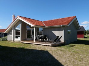 A single-story house with a red-tiled roof, a covered patio with outdoor furniture, and a large sliding glass door. - 4 Star Holiday Home in Grossenbrode (Grossenbrode)