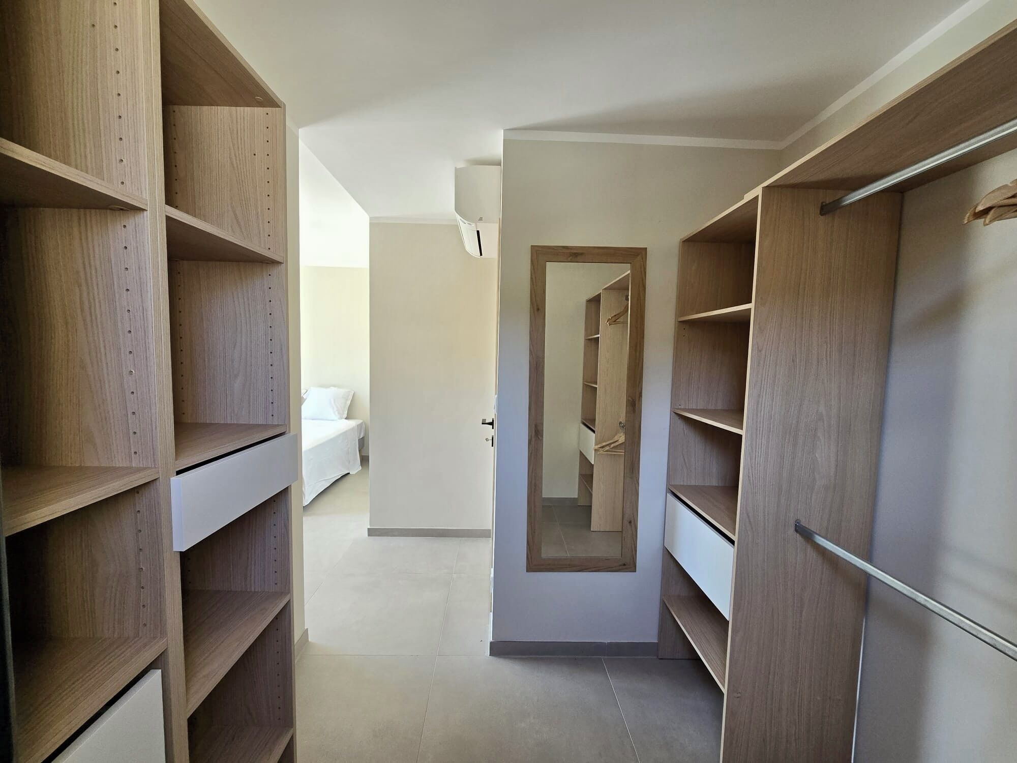 Un dressing accessible sans porte, doté d’étagères en bois et d’une porte de placard miroir.