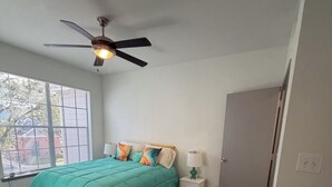 Een slaapkamer met een bed, een plafondventilator, een nachtkastje, een lamp, een raam en een kledingkast.