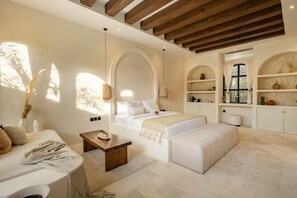 A spacious bedroom with a large bed, a sitting area with a table, and built-in shelving with decorative items. - Orivista Romantic 2 Private Suites + Pools Villa (Mengwi)