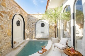 A stone-walled pool area with a white chair and a table, surrounded by large windows and a palm tree. - Orivista Romantic 2 Private Suites + Pools Villa (Mengwi)