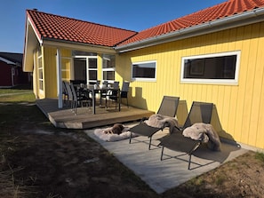 A yellow house with a red tiled roof, a deck with outdoor furniture, and a dog lying on the ground. - 4 Star Holiday Home in Grossenbrode (Grossenbrode)