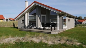A modern house with a red roof, a covered patio with outdoor furniture, and a visible chimney. - 4 Star Holiday Home in Grossenbrode (Grossenbrode)