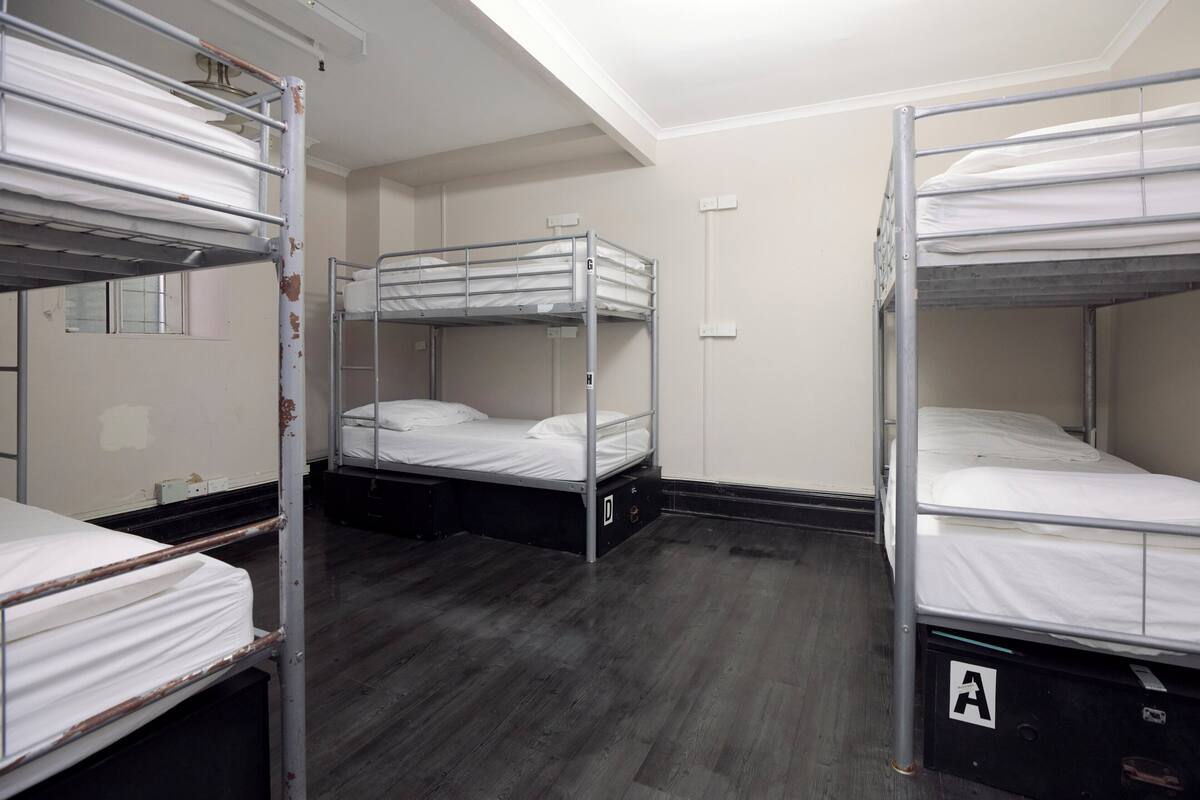 A room with bunk beds, a wooden floor, and a white wall.