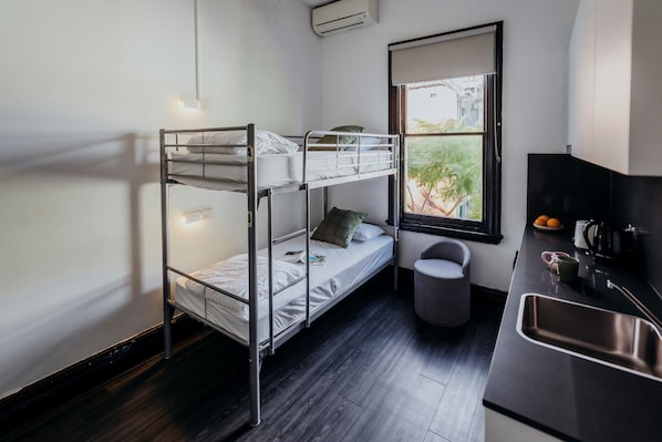 A bunk bed room with a window, a sink, and a small kitchen area. - Glebe Terraces (Glebe)