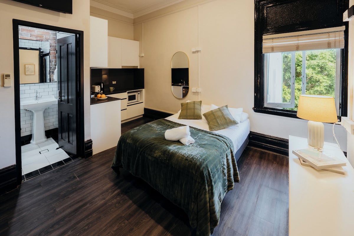 A hotel room with a bed, a desk, a mirror, a window, and a view of the outdoors.