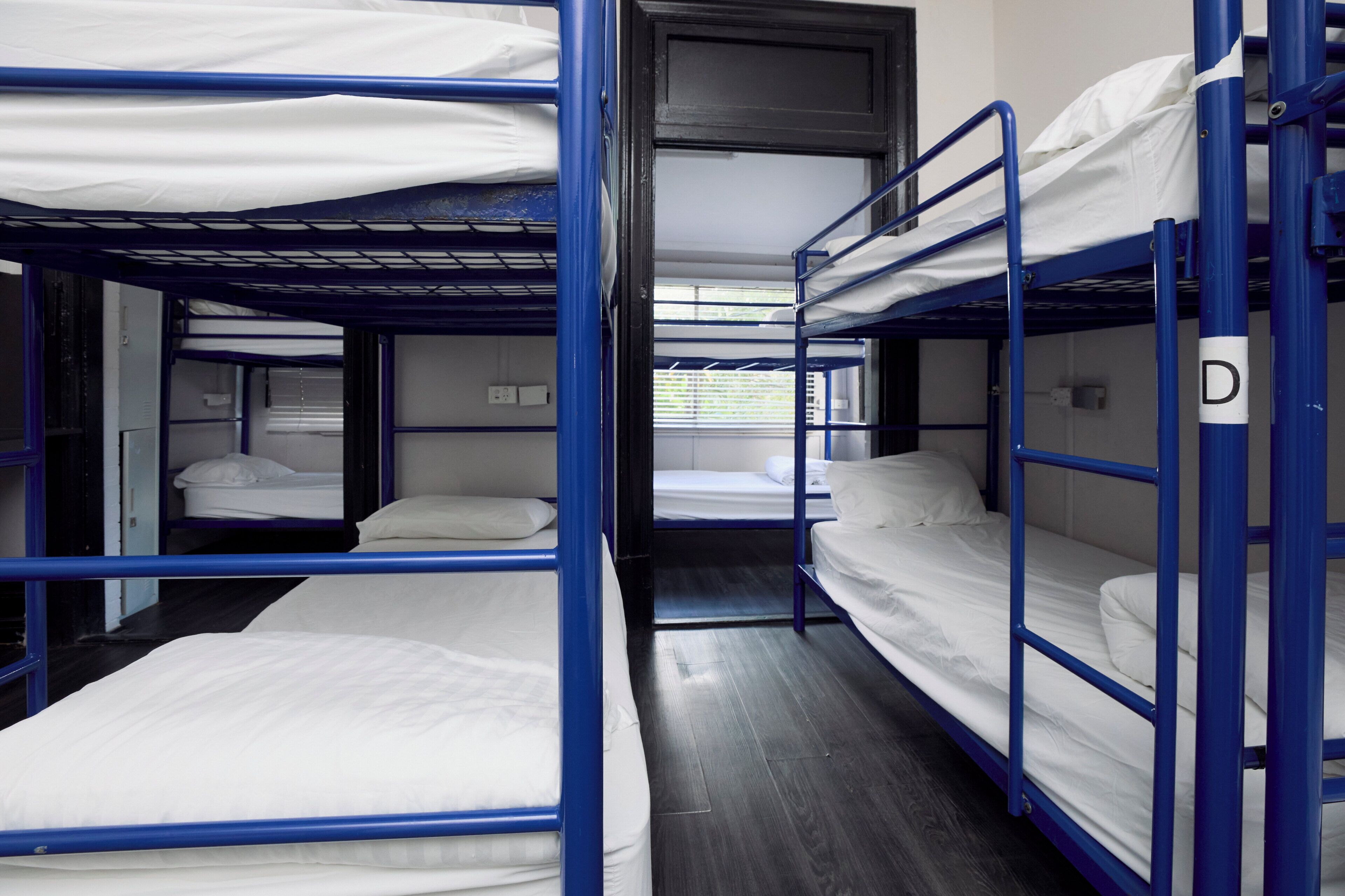 A bunk bed room with a wooden floor, a window with blinds, and a door.