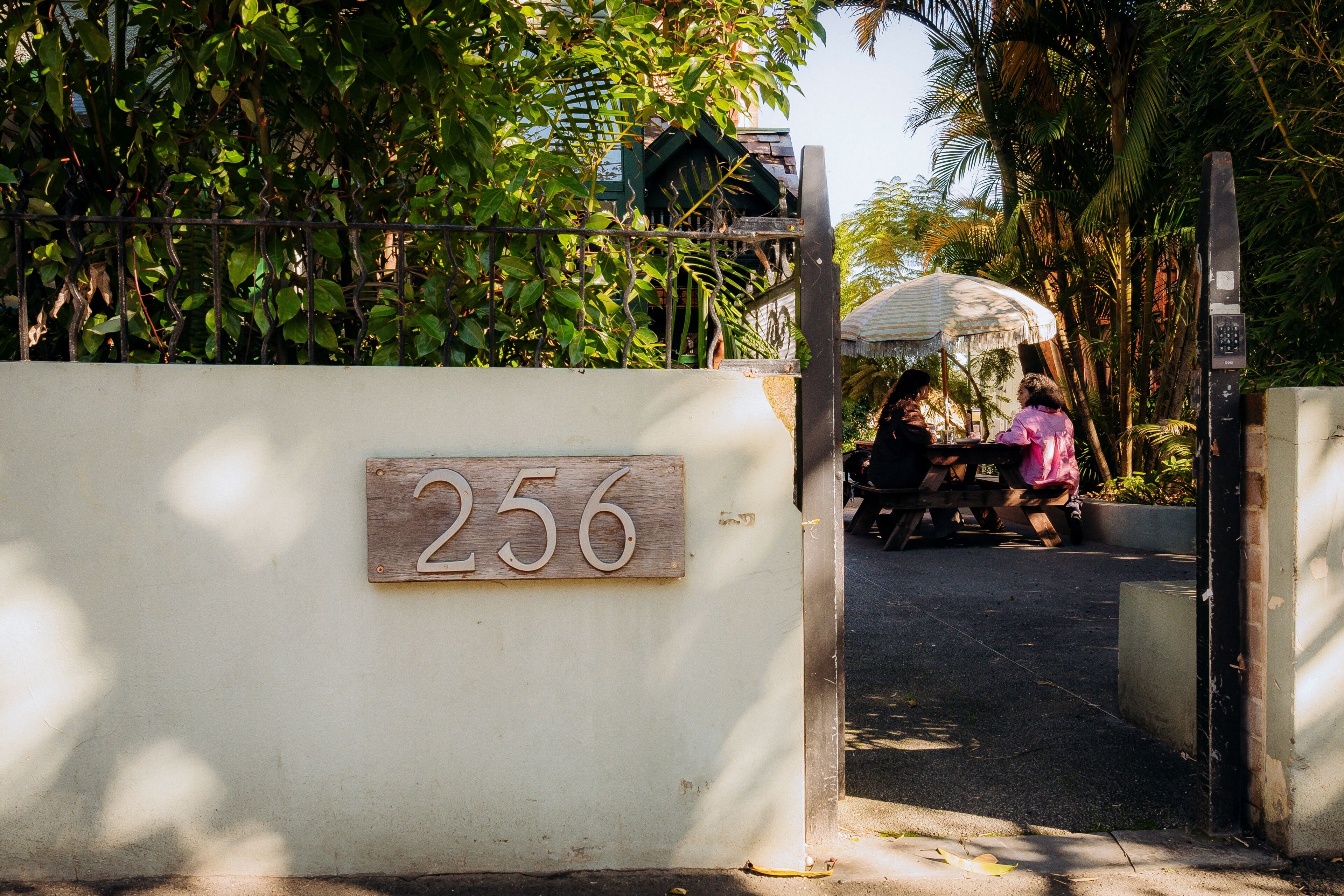 Une entrée fermée par un portail, sur laquelle est fixée une plaque en bois portant le numéro 256.