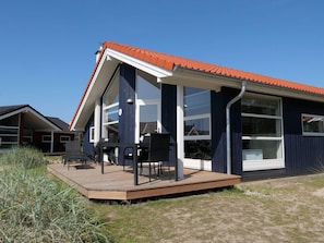 A modern house with a red roof, large windows, and a wooden deck with outdoor furniture. - 4 Star Holiday Home in Grossenbrode (Grossenbrode)