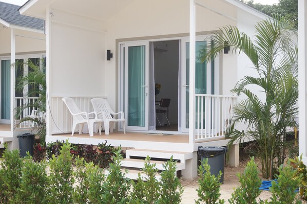 A covered outdoor area with white chairs, a small table, and a sliding glass door leading to a room.