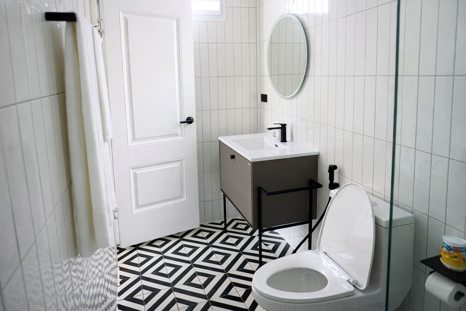 A bathroom with a white door, a sink, a toilet, and a patterned floor.