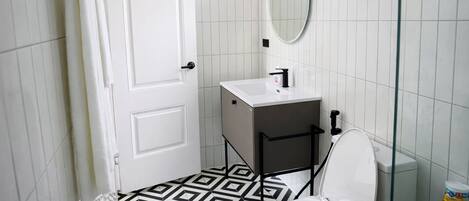 A bathroom with a white door, a sink, a toilet, and a patterned floor.